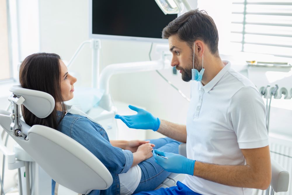 A woman sitting in a dental chair dicussing her concerns with her dentist.