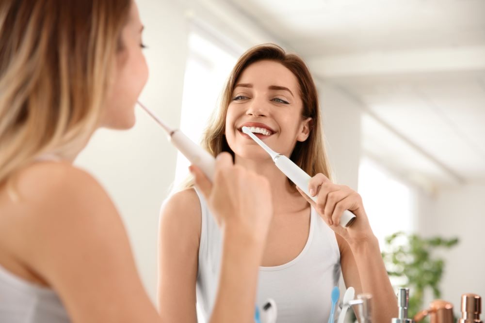 A woman smiling while brushing her teeth.