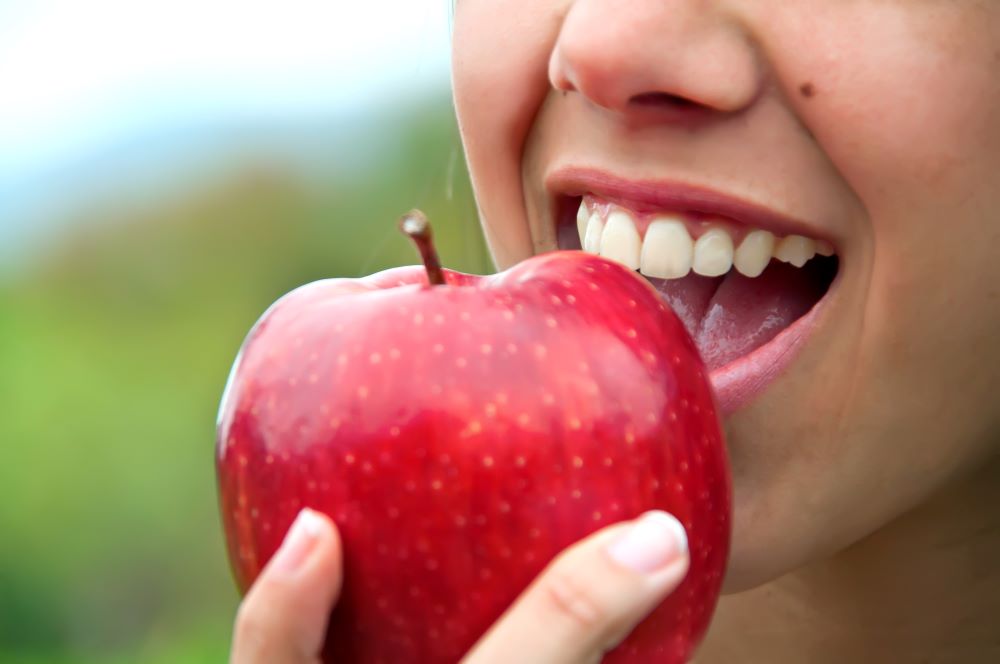 A woman biting into an apple to maintain her physical and dental health.