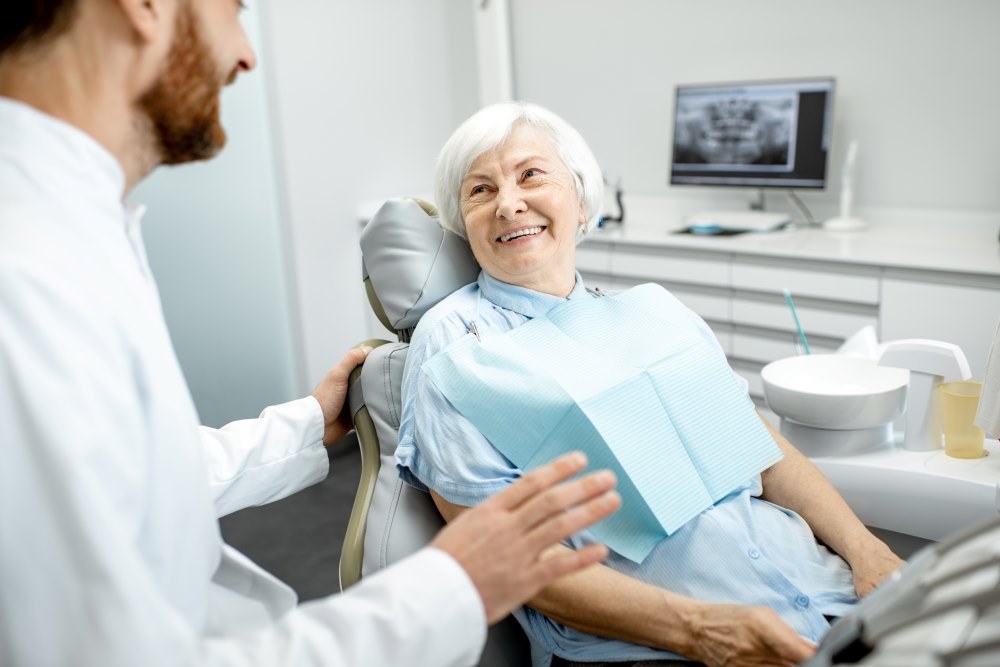 An elderly woman speaking with her dentist about her routine oral screening results.
