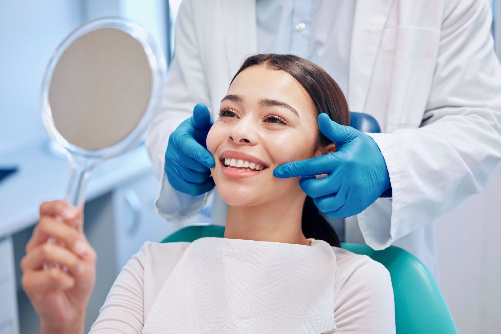 A woman looking at her teeth in the mirror after a teeth cleaning at a dental office.