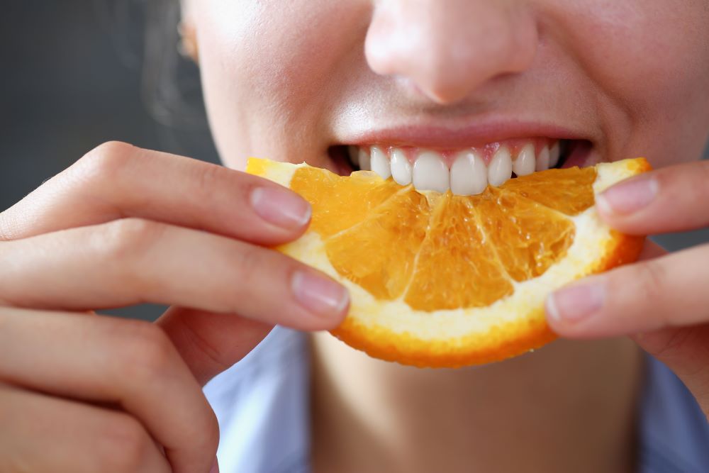 A woman smiling while eating an orange slice.