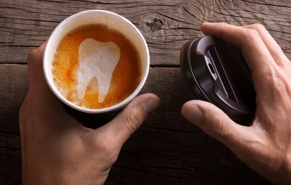 A man holding an open coffee cup with a tooth design in the froth as a visual that coffee stains teeth.