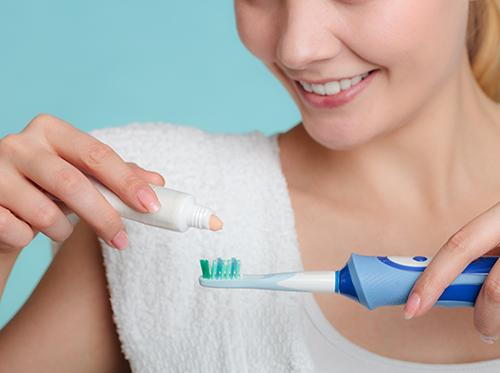 Woman putting toothpaste in electric toothbrush